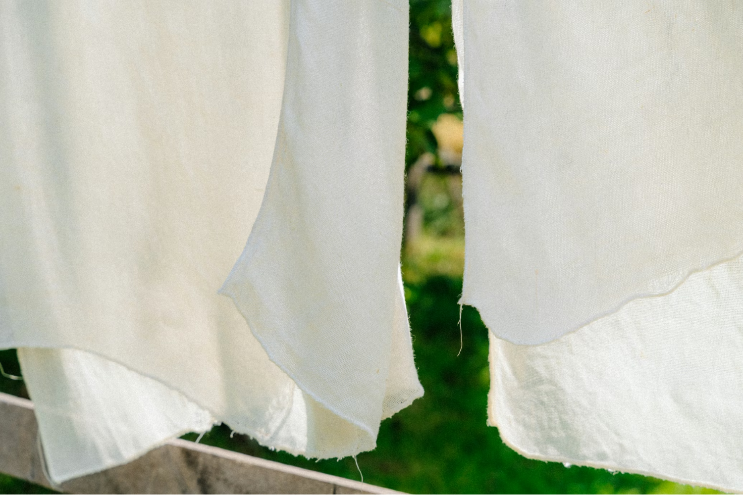 Close-up of white fabric pieces hanging outdoors, showing raw edges and natural texture.