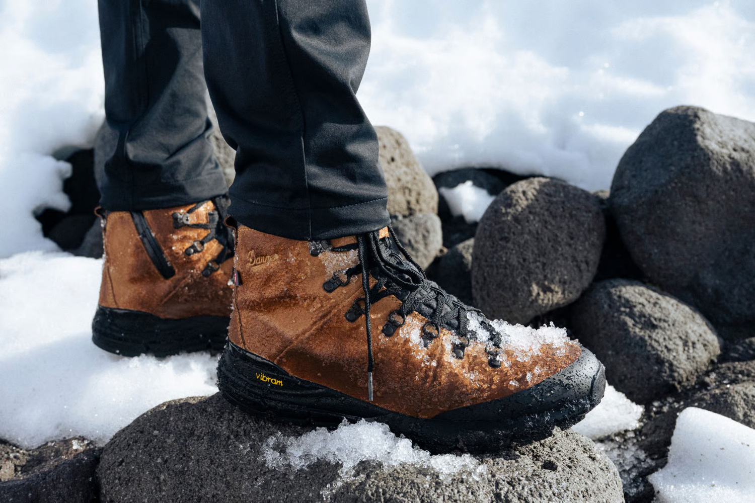 Person wearing brown sustainable hiking boots standing on snowy rocks