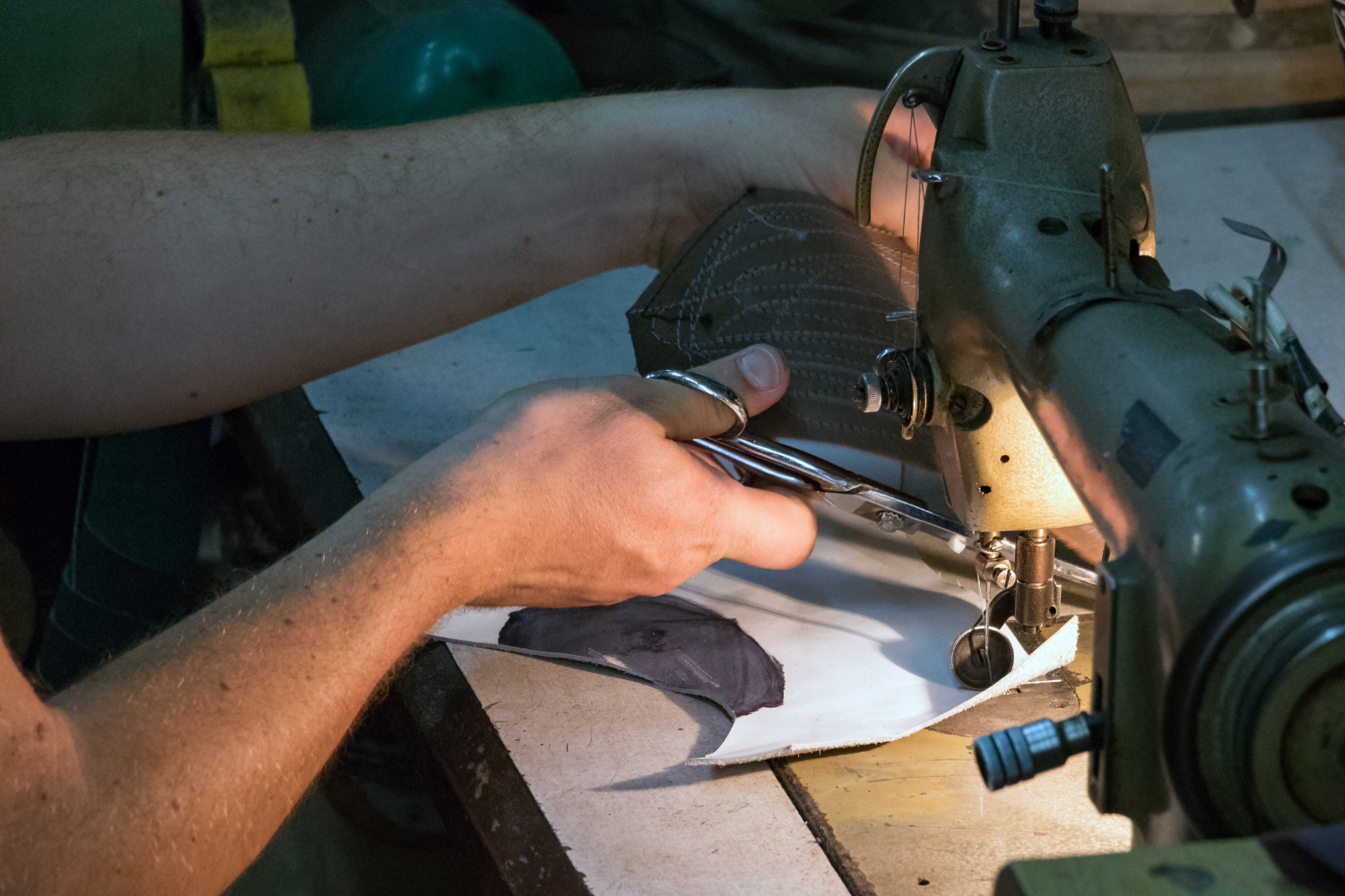 Close‑up of hands repairing a shoe using a sewing machine, highlighting shoe repair and extending footwear lifespan.