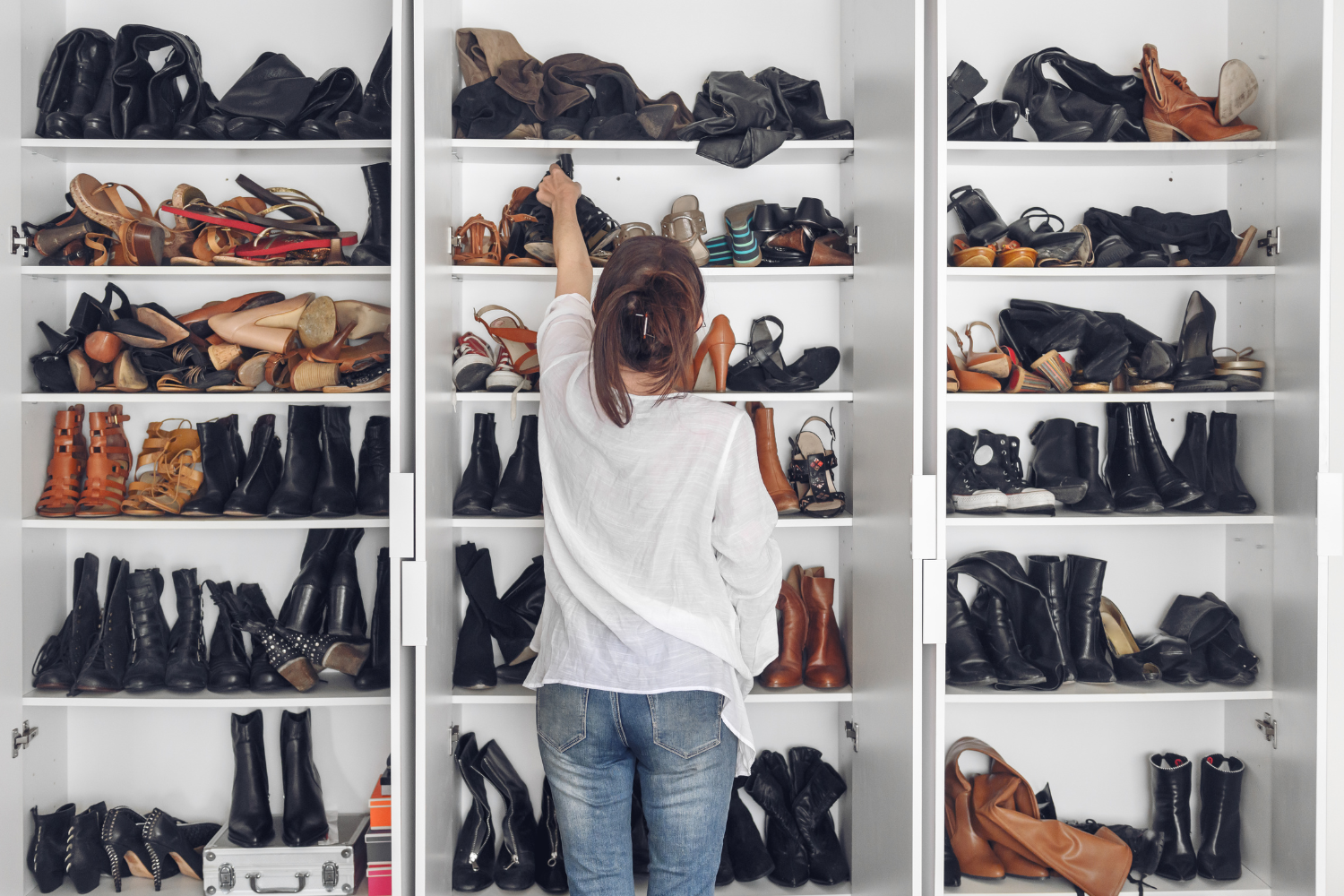 Person standing in front of an open wardrobe filled with shoes, reaching for a pair while decluttering their shoe collection.