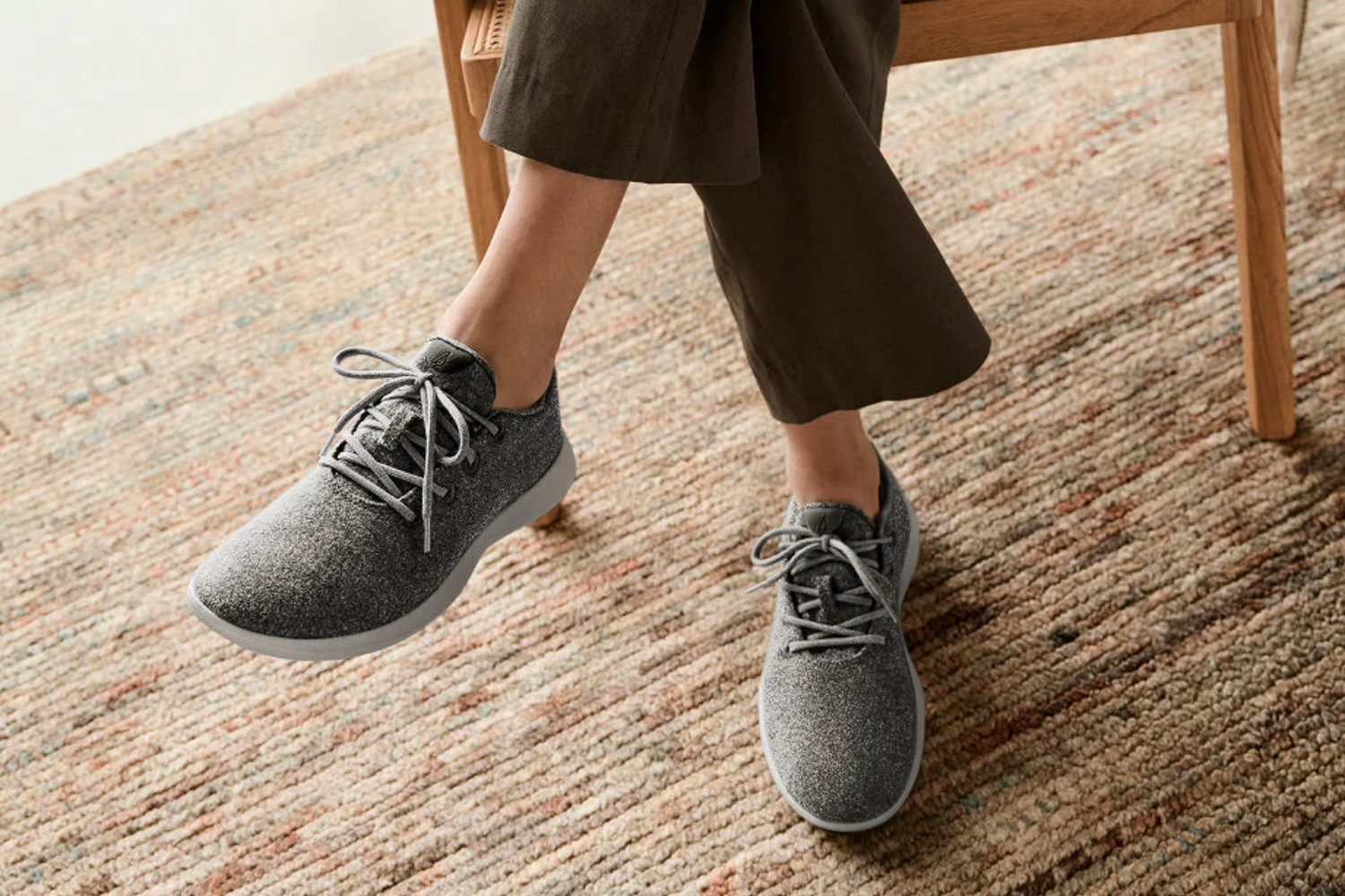 Close-up of a person wearing grey wool sneakers on a woven rug, symbolizing comfort, durability, and low-impact materials in modern footwear.
